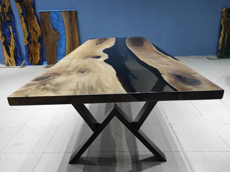 May include: A large wooden dining table with a black epoxy resin river flowing through the center. The table has a black metal X-shaped base.