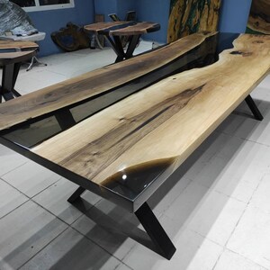 May include: A large wooden dining table with a black epoxy resin river running through the center. The table has a natural wood finish and black metal legs.