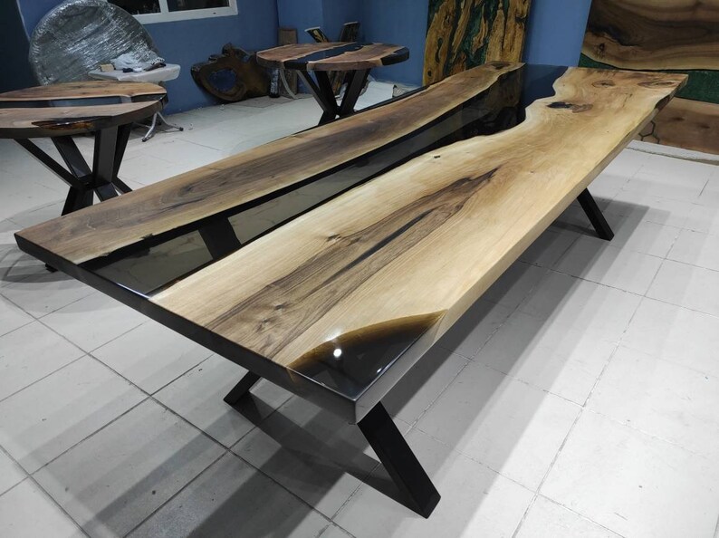 May include: A large wooden dining table with a black epoxy resin river running through the center. The table has a natural wood finish and black metal legs.