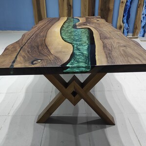 May include: A wooden dining table with a live edge top and a green epoxy river running through the center. The table has a dark brown wood finish and a metal X-shaped base.