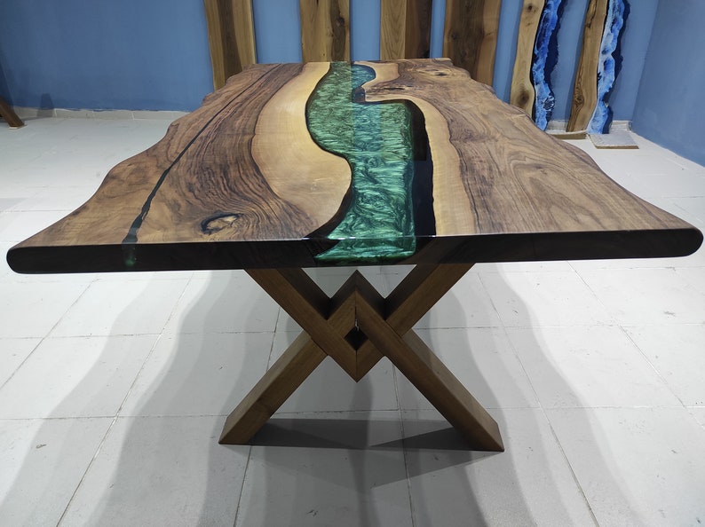 May include: A wooden dining table with a live edge top and a green epoxy river running through the center. The table has a dark brown wood finish and a metal X-shaped base.