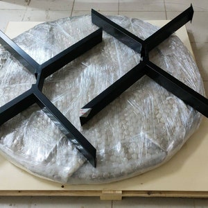 May include: Two black metal table bases, each with a four-pronged design, are shown on a wooden pallet. The bases are wrapped in clear plastic and are ready for shipping.