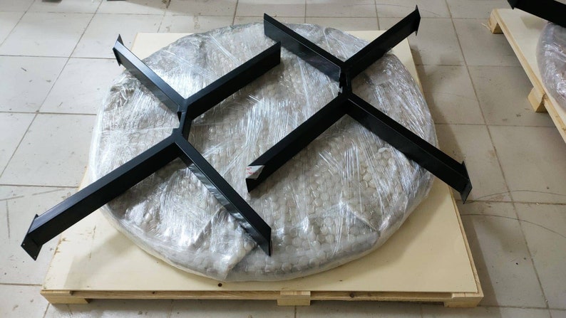 May include: Two black metal table bases, each with a four-pronged design, are shown on a wooden pallet. The bases are wrapped in clear plastic and are ready for shipping.