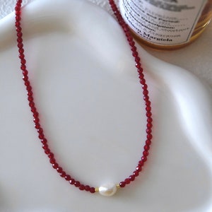 May include: A red crystal beaded necklace with a single white pearl pendant.