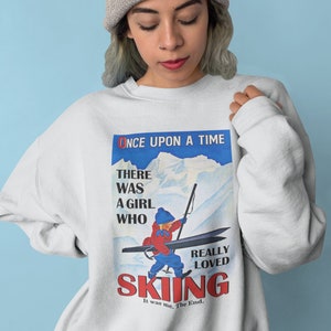 Pode incluir: Uma camisa de moletom branca com uma estampa gr&aacute;fica vintage de um esquiador. O gr&aacute;fico apresenta o texto "Once Upon A Time" e "There Was A Girl Who Really Loved Skiing".