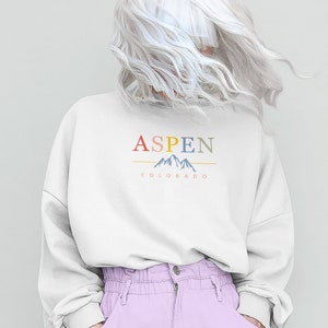 May include: A white sweatshirt with the text "ASPEN COLORADO" and a graphic of mountains in colorful hues.