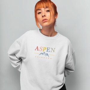 May include: A white sweatshirt with a colorful graphic design that says "ASPEN COLORADO" with a stylized mountain range.