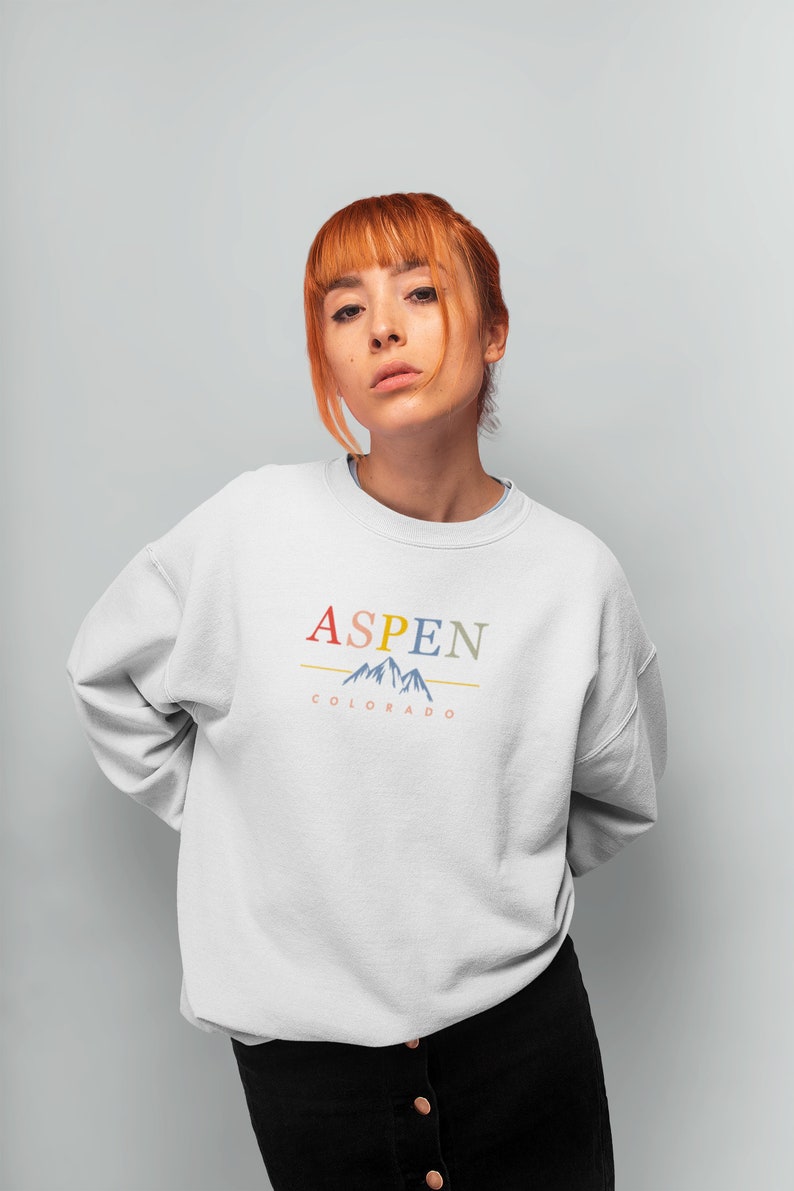 May include: A white sweatshirt with a colorful graphic design that says "ASPEN COLORADO" with a stylized mountain range.