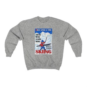 Pode incluir: Uma camisa de frio cinza com uma ilustra&ccedil;&atilde;o vintage de uma menina esquiando. A ilustra&ccedil;&atilde;o inclui o texto "Once Upon A Time There Was A Girl Who Really Loved Skiing. It was me. The End."