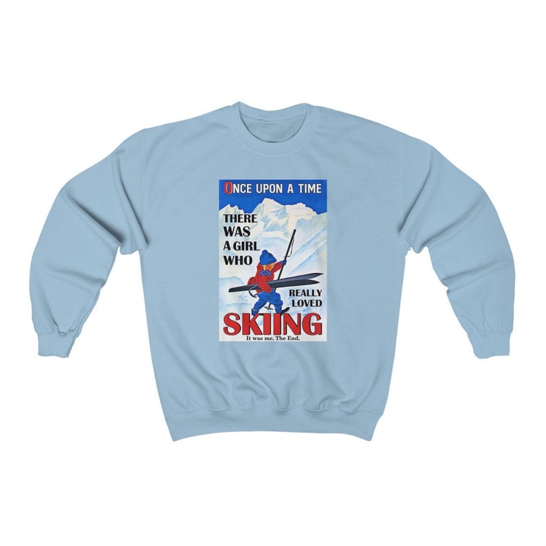 Pode incluir: Uma camisa de frio azul claro com uma ilustra&ccedil;&atilde;o vintage de uma menina esquiando. O texto diz "Era uma vez uma menina que realmente amava esquiar. Era eu. Fim."