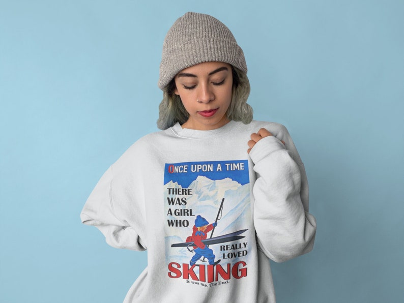 Pode incluir: Uma camisa de moletom branca com uma estampa gr&aacute;fica vintage de um esquiador. O gr&aacute;fico apresenta o texto "Once Upon A Time" e "There Was A Girl Who Really Loved Skiing".