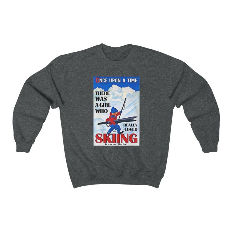 Pode incluir: Uma camisola cinzenta escura com uma ilustra&ccedil;&atilde;o vintage de uma menina a esquiar. A ilustra&ccedil;&atilde;o &eacute; num esquema de cores vermelho, azul e branco e apresenta o texto "Once Upon A Time There Was A Girl Who Really Loved Skiing It Was Me. The End."