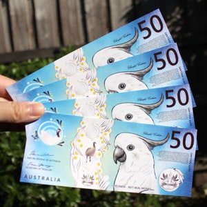 May include: Four Australian fifty dollar bills featuring a white cockatoo and the text "Nature Reserve of Australia" and "Secretary of Treasury". The bills are stacked on top of each other and are marked "Specimen - Not Real Money".