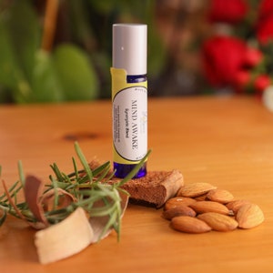 May include: A blue and yellow roller bottle with the label "MIND AWAKE Synergistic Blend" on a wooden surface with almonds and rosemary sprigs.