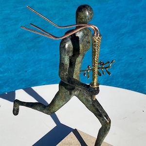 May include: Bronze sculpture of a running figure holding a torch and olive branch. The figure has a green patina and copper accents. The sculpture is mounted on a square stone base, with a blue background.
