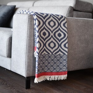 May include: A grey sofa with a blue and white patterned throw blanket with a red fringe. The blanket has a geometric design.