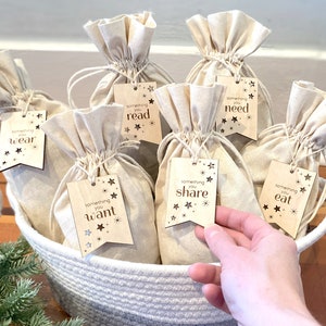 May include: A white wicker basket filled with small white fabric bags. Each bag has a wooden tag attached with a gold star design and text that reads "something you wear", "something you read", "something you need", "something you want", "something you share", and "something you eat".