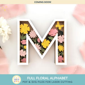 May include: A white letter 'M' filled with yellow and pink flowers and a yellow butterfly. The text 'COMING SOON!' is at the top, and 'FULL FLORAL ALPHABET' and 'PDF & SVG FILES FOR LASER CUTTING' are at the bottom.