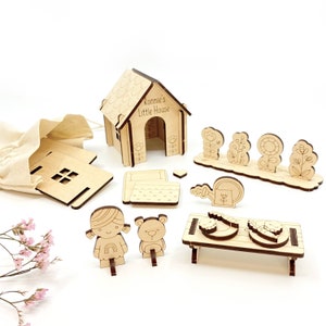May include: A wooden playset for children, featuring a house, a bed, a table, a watering can, flowers, a girl doll, and a bear doll. The house has the text "Ronnie's Little House" on the front.