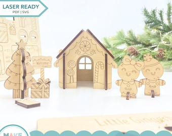 May include: A laser-ready 3D Christmas gingerbread house kit with SVG and PDF files. The kit includes a house, two gingerbread people, a Christmas tree, and gifts. The house has a brown roof and decorative details. The gingerbread people have smiling faces.