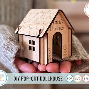 May include: A wooden dollhouse kit with a pop-out design. The dollhouse is light brown and has a roof with a scalloped edge. The dollhouse has a front door and a window. The text "Ronnie's Little House" is engraved on the front of the dollhouse.