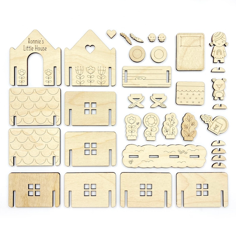 May include: A wooden craft kit for building a house with a personalized name, "Ronnie's Little House". The kit includes various pieces for the house, roof, windows, doors, and a garden with flowers, trees, a watering can, a fence, a beehive, a swing set, a pool, a bear, and a girl.