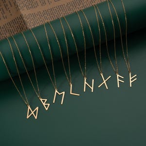 May include: A set of ten gold necklaces with different rune symbols as pendants. The necklaces are displayed against a green background.