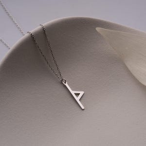 May include: A silver chain necklace with a pendant shaped like the letter 'A'. The pendant is made of a single piece of metal and has a simple, modern design.