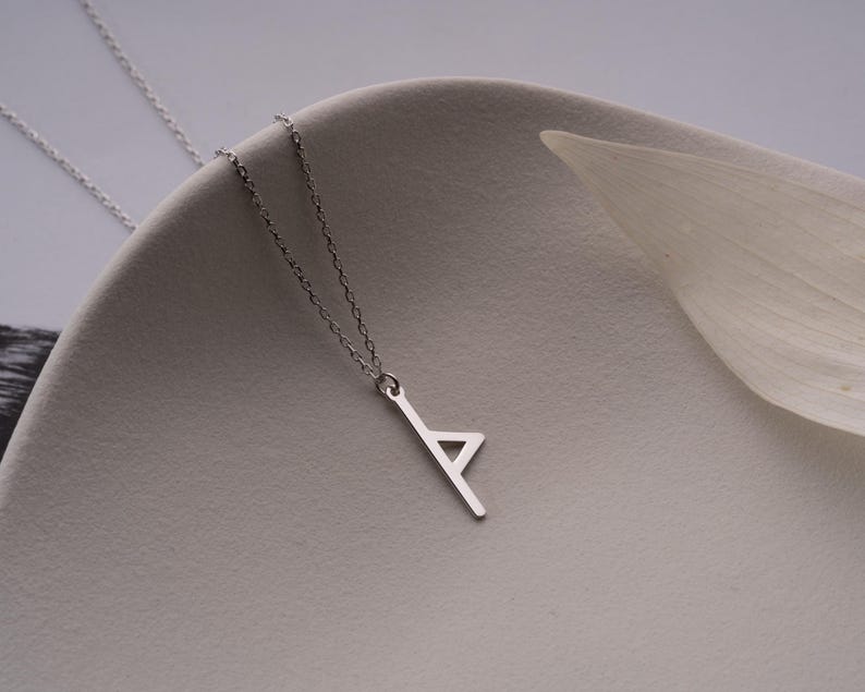 May include: A silver chain necklace with a pendant shaped like the letter 'A'. The pendant is made of a single piece of metal and has a simple, modern design.