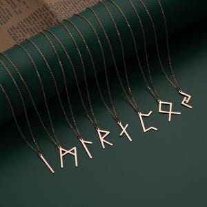 May include: A set of ten delicate gold necklaces with different rune symbols as pendants. The necklaces are arranged on a green background.