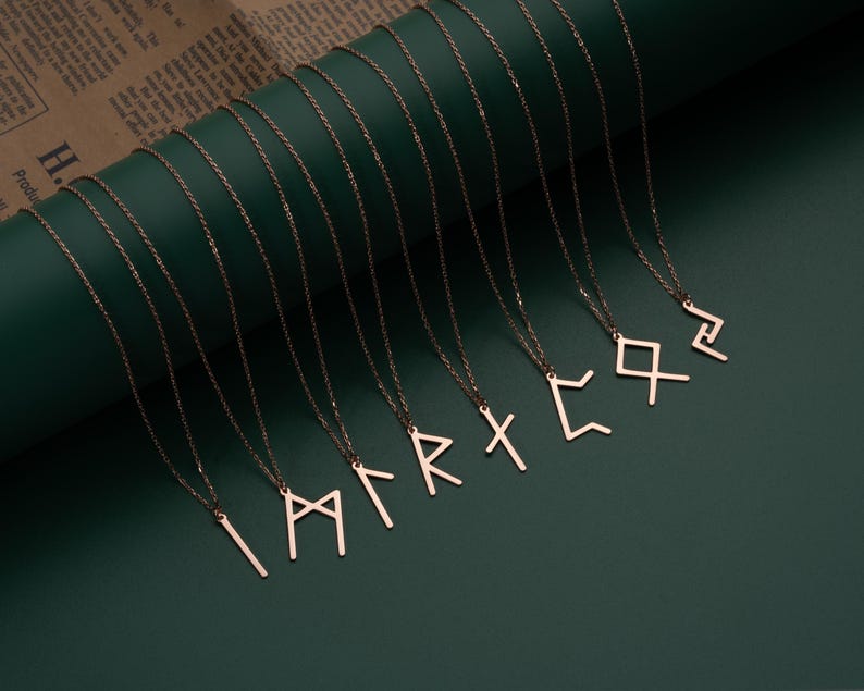 May include: A set of ten delicate gold necklaces with different rune symbols as pendants. The necklaces are arranged on a green background.