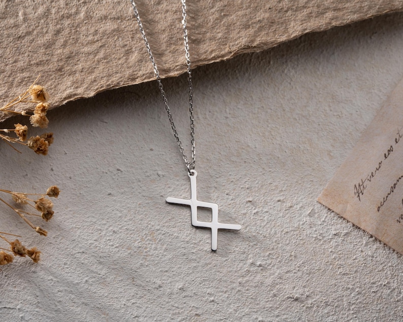 May include: A silver chain necklace with a geometric pendant in the shape of a cross. The pendant is made of a single piece of metal and has a simple, modern design.
