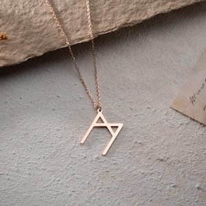 May include: A rose gold necklace with a geometric pendant shaped like the letter 'M'.
