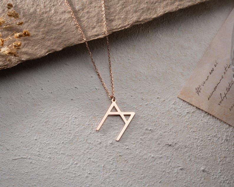 May include: A rose gold necklace with a geometric pendant shaped like the letter 'M'.