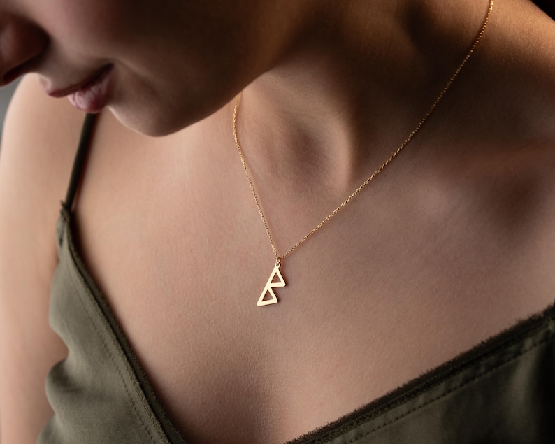 May include: A gold necklace with a geometric triangle pendant. The pendant is made of two overlapping triangles.