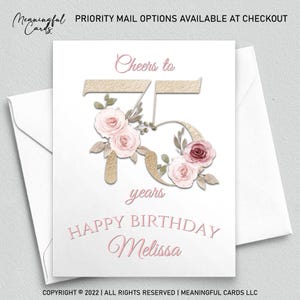 May include: A white birthday card with a floral design and the text "Cheers to 75 years Happy Birthday Melissa". The card features a gold-colored "75" with pink roses and greenery. The card is inside a white envelope.