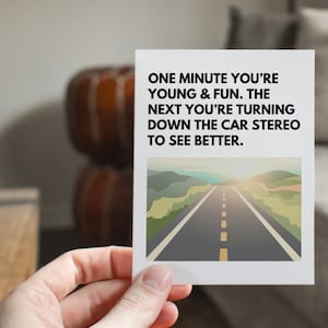 May include: A white card with a black and white text overlay. The text reads "ONE MINUTE YOU'RE YOUNG & FUN. THE NEXT YOU'RE TURNING DOWN THE CAR STEREO TO SEE BETTER." The card has a photo of a road with a sunset in the background.