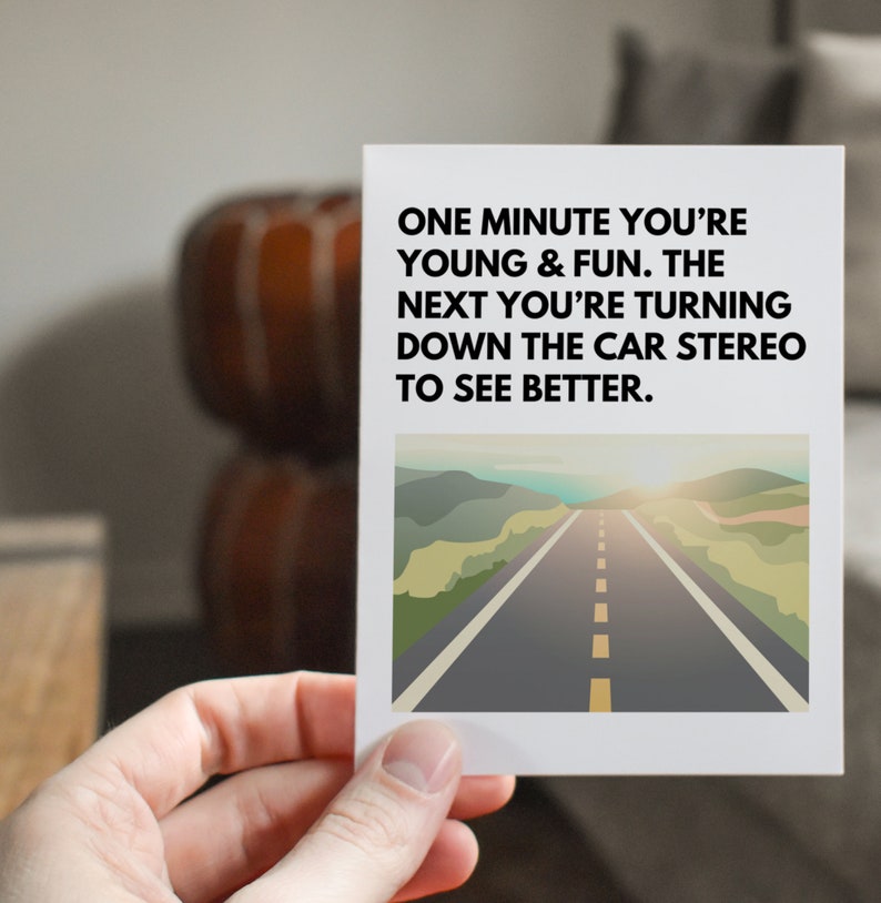 May include: A white card with a black and white text overlay. The text reads "ONE MINUTE YOU'RE YOUNG & FUN. THE NEXT YOU'RE TURNING DOWN THE CAR STEREO TO SEE BETTER." The card has a photo of a road with a sunset in the background.