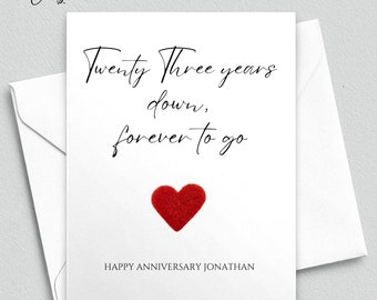 May include: A white card with black calligraphy that reads "Twenty Three years down, forever to go". A red felt heart is in the center of the card. The text "HAPPY ANNIVERSARY JONATHAN" is at the bottom of the card.