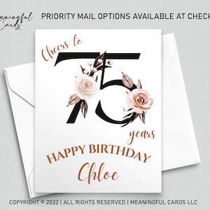 May include: A white card with a black number 75 decorated with pink and brown floral illustrations. The text "Cheers to" is above the number and "years" is below the number. The text "HAPPY BIRTHDAY Chloe" is below the number.