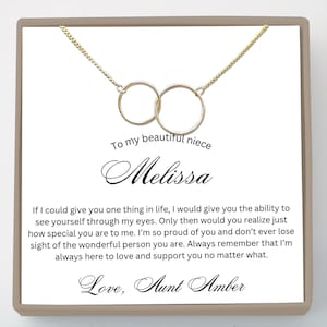 May include: A gold-colored necklace with two interlocking circles, presented on a white card. The card includes the text "To my beautiful niece Melissa" and a heartfelt message from "Aunt Amber."