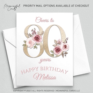 May include: A white birthday card with a gold-textured "80" and floral accents in pink and burgundy. The card reads "Cheers to 80 years" and "Happy Birthday Melissa" in a delicate pink script. Includes a white envelope.