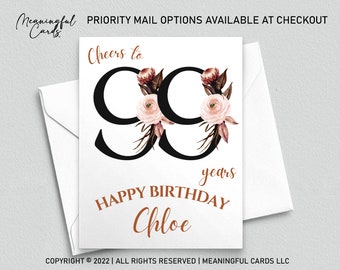 Op de afbeelding: Een witte kaart met zwarte tekst en een bloemmotief. De tekst luidt "Cheers to 99 years Happy Birthday Chloe".