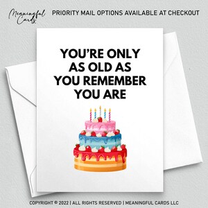 Op de afbeelding: Een witte wenskaart met de tekst "YOU'RE ONLY AS OLD AS YOU REMEMBER YOU ARE" en een kleurrijke verjaardagstaart illustratie. De taart heeft meerdere lagen met roze, blauwe en rode glazuur, gegarneerd met aardbeien en brandende kaarsen. De kaart zit in een witte envelop.