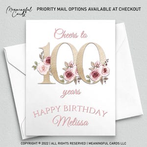 May include: A white birthday card with a gold "100" and floral accents. The card reads "Cheers to 100 years" and "Happy Birthday Melissa" in pink script. The card is inside a white envelope.
