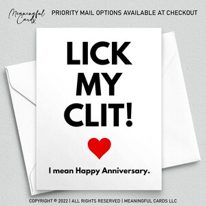 May include: A white card with black text that reads "LICK MY CLIT!" with a red heart below the text. The text below the heart reads "I mean Happy Anniversary."