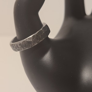 A worn hand-forged black steel ring on a mannequin's thumb.