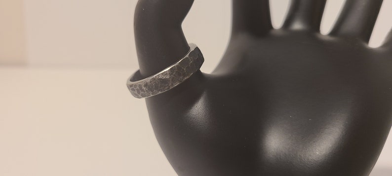 A worn hand-forged black steel ring on a mannequin's thumb.