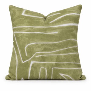 May include: A square throw pillow in a muted olive green shade featuring a hand-painted style pattern of irregular, thin white lines that traverse the surface in various horizontal and angular directions across the fabric cover.