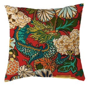 May include: Square decorative pillow with a vibrant red background and a detailed dragon and floral pattern. The dragon is teal, green, and yellow, surrounded by cream and orange flowers and green leaves. A decorative accent for a sofa or bed.